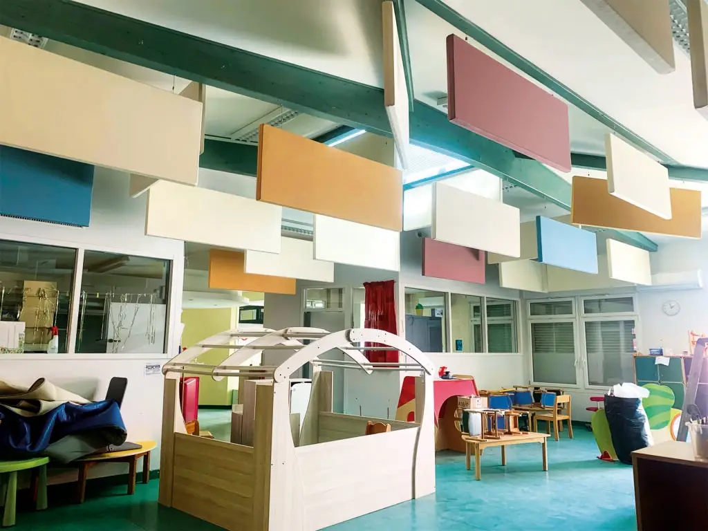 Panneau acoustique breveté Matoileperso, de forme ludique et colorée, fixé au mur d’une crèche pour réduire le bruit ambiant. Des enfants jouent dans une pièce lumineuse, le panneau ajoute une touche décorative tout en améliorant le confort sonore de l’espace.