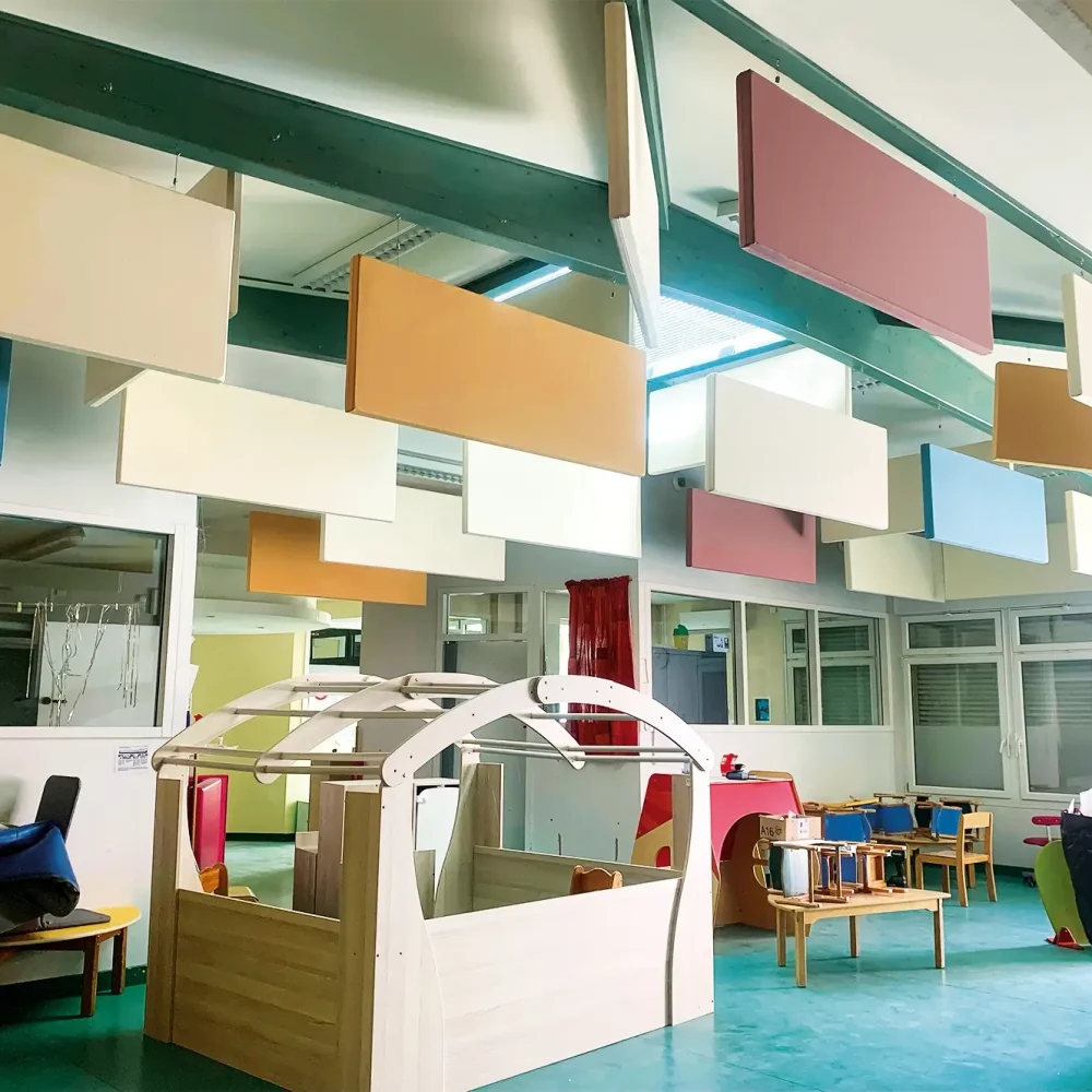 Panneau acoustique breveté Matoileperso, de forme ludique et colorée, fixé au mur d’une crèche pour réduire le bruit ambiant. Des enfants jouent dans une pièce lumineuse, le panneau ajoute une touche décorative tout en améliorant le confort sonore de l’espace.