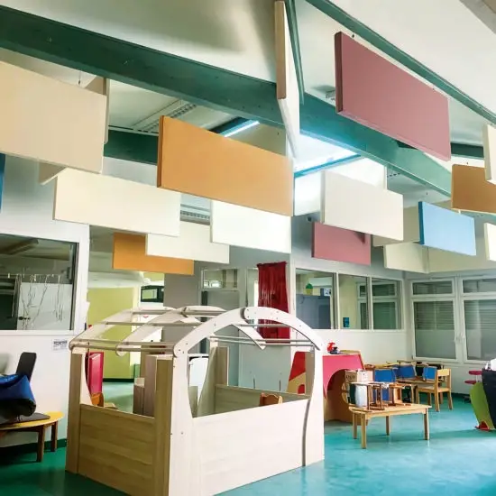 Panneau acoustique breveté Matoileperso, de forme ludique et colorée, fixé au mur d’une crèche pour réduire le bruit ambiant. Des enfants jouent dans une pièce lumineuse, le panneau ajoute une touche décorative tout en améliorant le confort sonore de l’espace.