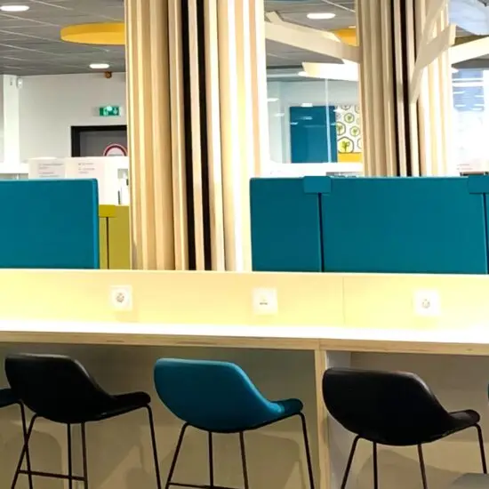 Open space moderne avec plusieurs bureaux partagés, équipé de panneaux acoustiques suspendus au plafond et de cloisons phonoabsorbantes colorées entre les postes de travail pour réduire le bruit. Des employés travaillent dans un environnement lumineux et calme, amélioré par les solutions acoustiques.
